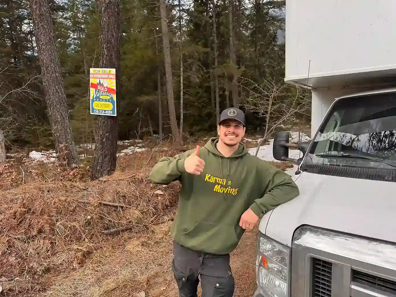 Moving company employee in front of truck giving thumbs up outdoors.